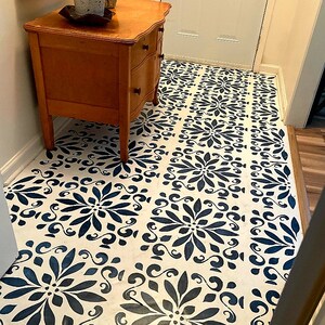 May include: A white floor with a blue and white stencil pattern. A wooden dresser with three drawers is in the corner of the room.