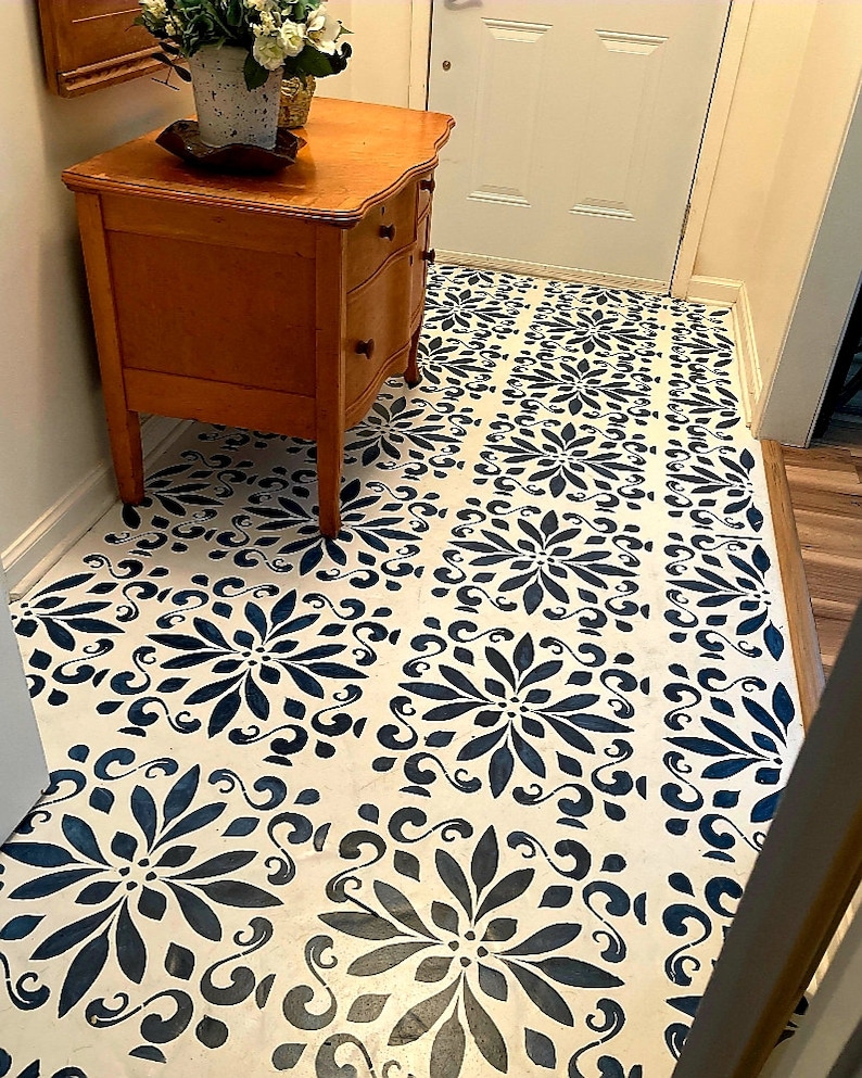 May include: A white floor with a blue and white stencil pattern. A wooden dresser with three drawers is in the corner of the room.