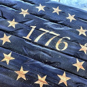May include: A wooden sign with a distressed blue background and gold stars. The year 1776 is carved into the wood.