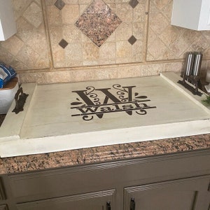 May include: A white wooden serving tray with a brown monogram of the letter "W" and the name "Walsh" in a decorative font. The tray has two metal handles on the sides.