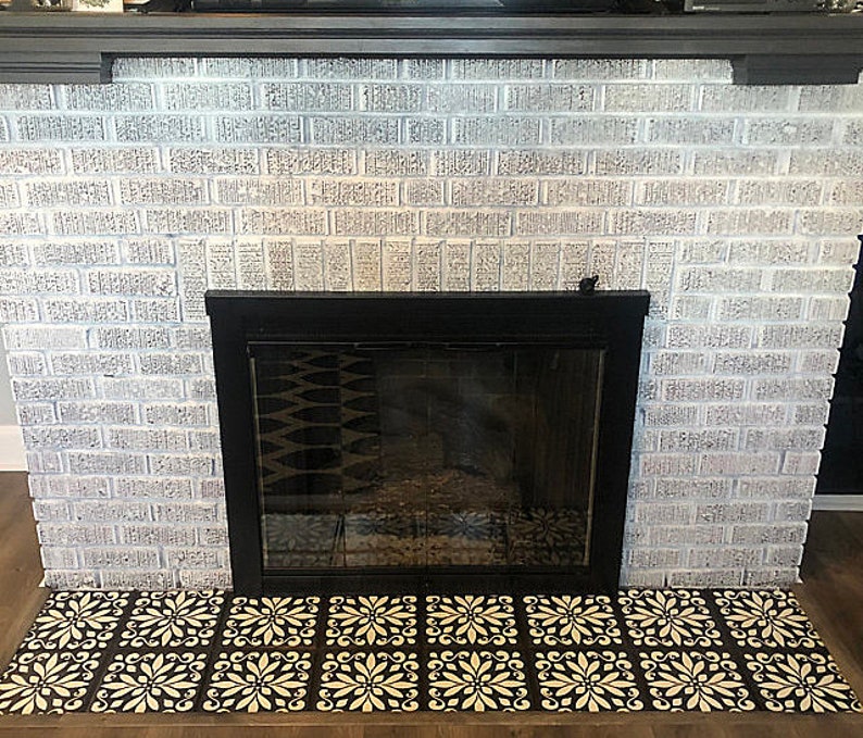 May include: A white brick fireplace with a black metal fireplace screen and a decorative tile hearth. The tiles are black with a white floral pattern.