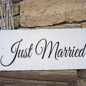 May include: White wooden sign with distressed paint and black cursive lettering that reads "Just Married".