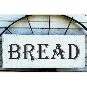 May include: A white wooden sign with black lettering that reads "BREAD". The sign has a rustic, farmhouse style.