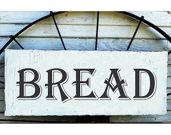May include: A white wooden sign with black lettering that reads "BREAD". The sign has a rustic, farmhouse style.
