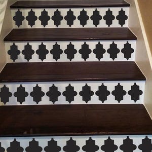 May include: A set of dark brown wooden stairs with black and white stencil designs on each step. The stencil design is a repeating pattern of quatrefoils.