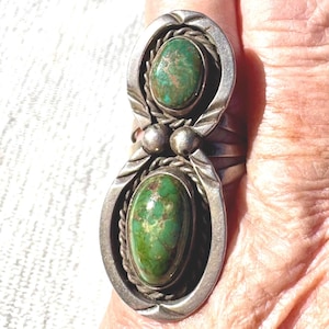 May include: A sterling silver ring featuring two oval-shaped green turquoise stones set vertically. The metalwork includes twisted wire detailing around each stone and a smooth, polished silver frame with etched leaf-like accents.