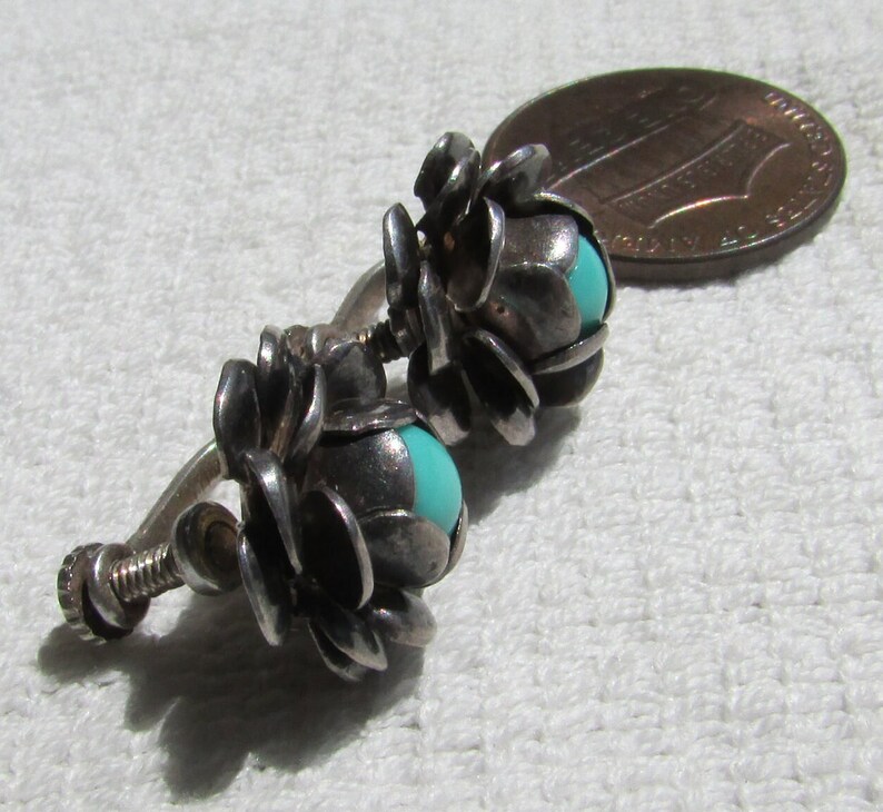 May include: A pair of silver clip-on earrings with turquoise stones set in the center of each flower-shaped design.