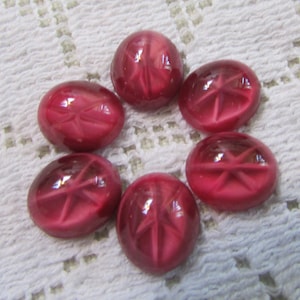 May include: Six oval-shaped, ruby-red glass buttons arranged in a circle. Each button has a starburst design etched into the center. The buttons are glossy and appear to be vintage or antique.