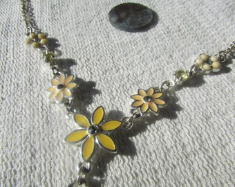May include: A silver chain necklace with yellow and white flower charms. The flowers have a light yellow enamel finish and a silver center.
