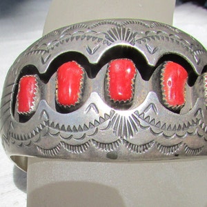 May include: A silver bracelet with a detailed design and five red coral stones.