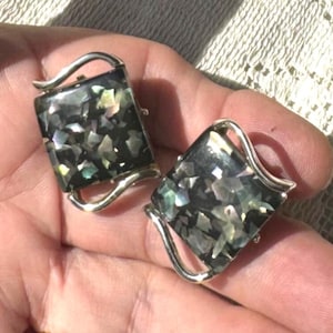 May include: A pair of vintage rectangular cufflinks with a shimmering abalone shell inlay. The iridescent shell pieces are set in a dark background, framed by a silver-toned metal with a curved design.