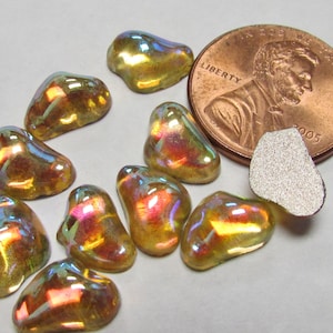 May include: A collection of iridescent, pebble-shaped glass beads in shades of gold, purple, and green. A U.S. penny is included for size reference, along with a small, silver, textured piece. The beads have a glossy finish and irregular shapes.