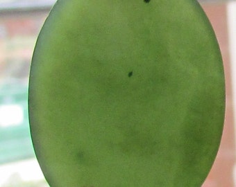 May include: A smooth, oval-shaped green stone with dark green inclusions. The stone is translucent and has a polished finish.