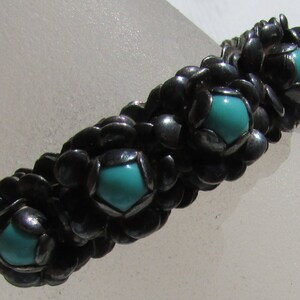 May include: A silver bracelet with turquoise stones set in a flower-like design.