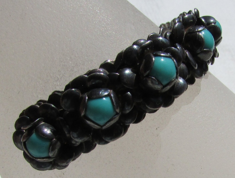 May include: A silver bracelet with turquoise stones set in a flower-like design.