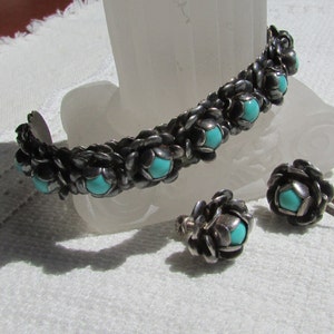 May include: A silver bracelet and earrings set with turquoise stones. The bracelet is made of a woven design with a row of turquoise stones. The earrings are also made of a woven design with a single turquoise stone.