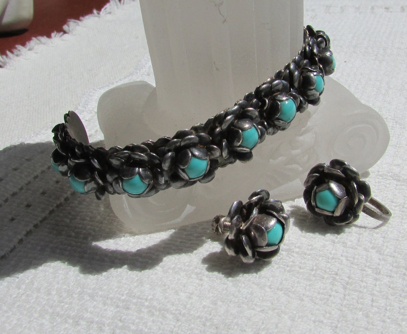 May include: A silver bracelet and earrings set with turquoise stones. The bracelet is made of a woven design with a row of turquoise stones. The earrings are also made of a woven design with a single turquoise stone.