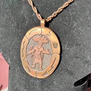 May include: A copper pendant necklace with a rope chain. The pendant features a circular design with an embossed image of a Native American figure in a traditional headdress.