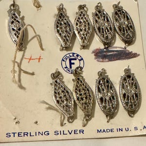 May include: A collection of sterling silver filigree clasps on a vintage card. The clasps are oval-shaped with intricate openwork designs. The card reads "STERLING SILVER" and "MADE IN U.S.A."