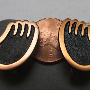 Pode incluir: Um par de brincos de cobre com um design de esmalte preto. Os brincos têm a forma de uma mão com cinco dedos.