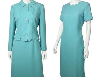 May include: A two-piece set consisting of a turquoise jacket and a matching short-sleeved dress. The jacket features a scalloped collar, three decorative buttons, and a scalloped hem. The dress has a matching scalloped neckline and short sleeves.