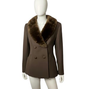May include: A double-breasted brown blazer featuring a wide, dark brown faux fur shawl collar. The jacket has long sleeves, a tailored fit, and four matching brown buttons arranged in two vertical rows on the front of the garment.