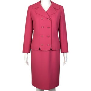 May include: A solid dark pink two-piece suit consisting of a double-breasted blazer and a matching knee-length skirt. The blazer features a wide notched collar, long sleeves, and four circular buttons arranged in two vertical rows on the front.