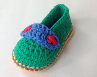 Può includere: Scarpe da bebé in crochet verde con un cinturino blu e bottoni rossi. Le scarpe hanno un bordo giallo e rosso.