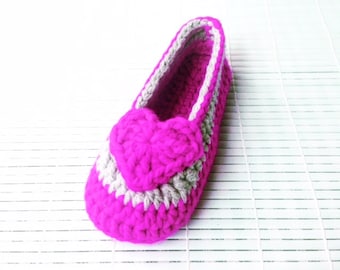 Può includere: Pantofola rosa in crochet con un dettaglio a forma di cuore grigio. La pantofola è su uno sfondo bianco.