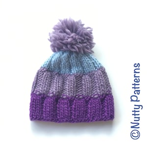 May include: A purple, blue, and light blue knitted hat with a purple pom pom on top.  The hat is made with a chunky yarn and has a ribbed texture.