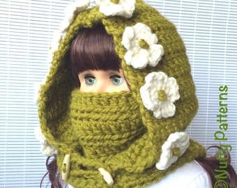 Può includere: Una sciarpa con cappuccio di lana verde con fiori bianchi all'uncinetto. La sciarpa ha un bottone e un bottone in legno.
