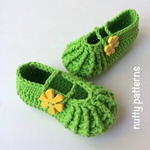 Peut inclure: Une paire de chaussons pour bébé en crochet vert avec des boutons en forme de fleurs jaunes. Les chaussons ont un design simple et sont parfaits pour les premiers pas d'un bébé.