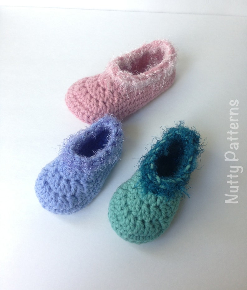 May include: Three pairs of crocheted baby booties in pink, blue, and green. Each bootie has a fluffy trim around the top.