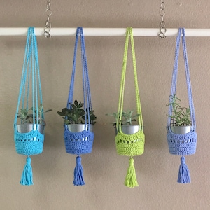 May include: Four macrame plant hangers with green plants in them. The hangers are made of blue and green yarn and have tassels at the bottom.