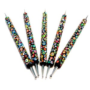 May include: Five black dotting tools with patterned handles. The handles are decorated with circles in red, yellow, blue, green, and orange. Each tool has a silver metal tip with a different end, including a pointed tip and a ball tip.