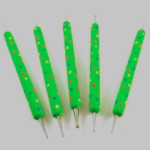 May include: Five green dotting tools with colorful polka dots. Each tool has a metal tip and a rounded handle. The tools are arranged in a fan shape against a light gray background, suitable for nail art or crafts.