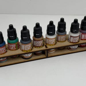 May include: A wooden rack with ten small bottles of paint. The bottles are labeled "Green Stuff World" and have black caps. The rack is designed to hold the bottles upright.