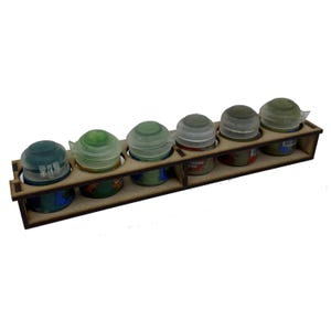 May include: A wooden paint pot holder with six paint pots. The paint pots are filled with various shades of green and blue paint. The paint pots have clear plastic lids. The holder is made of light brown wood.