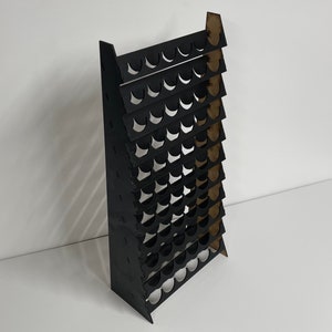May include: Black acrylic paint rack with multiple rows of circular cutouts for holding paint bottles.