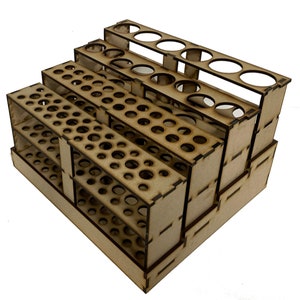 May include: Wooden paint pot holder with multiple tiers and rows of circular holes for storing paint tubes. The holder is made of unfinished wood and is designed to hold a variety of paint sizes.