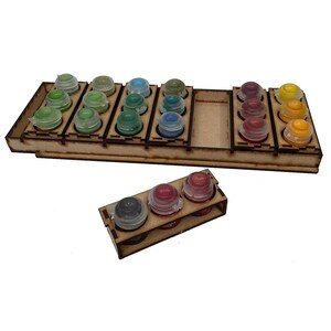 May include: A wooden paint bottle organizer with multiple slots holding various colors of paint bottles. The bottles have clear lids and are filled with shades of green, blue, red, and yellow paint. A smaller organizer with three bottles is also present.