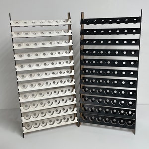 May include: Two wooden display stands with rows of circular holes. The stand on the left is white and the stand on the right is black.