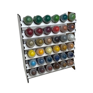 Puede incluir: Un organizador blanco de botellas de pintura de varios niveles, lleno de botellas de pintura de varios colores. El organizador es de madera y tiene varios estantes para guardar las botellas. Las botellas de pintura están dispuestas en filas y columnas, mostrando una variedad de colores.