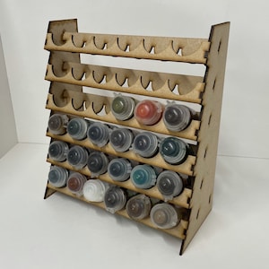May include: Wooden paint rack with multiple shelves for storing paint bottles. The rack is made of light brown wood and has a total of 7 shelves. The shelves are filled with various colours of paint bottles.