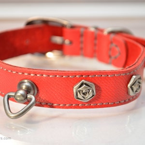 May include: Red leather dog collar with silver metal accents and a rose design. The collar has a silver metal D-ring and a silver metal buckle.