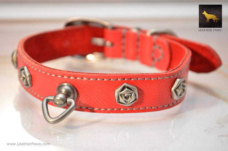 May include: Red leather dog collar with silver metal accents and a rose design. The collar has a silver metal D-ring and a silver metal buckle.