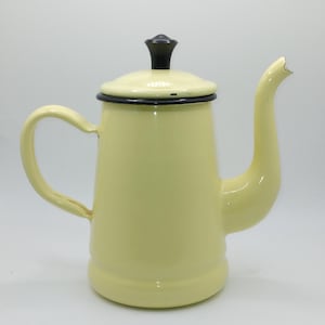 May include: A pale yellow enamelware coffee pot with a black handle and lid finial. The pot has a curved spout and a rounded handle. The lid is also pale yellow with a black rim. The pot is designed for brewing coffee.