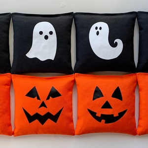 May include: Eight Halloween-themed bean bags. Four bean bags are black with white ghost designs. Four bean bags are orange with black jack-o'-lantern designs.