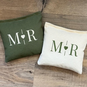 May include: Two rectangular fabric pouches, one olive green and one off-white. The olive pouch features white lettering M and R separated by a vertical line and a small heart. The off-white pouch features olive green lettering M and R with a heart.