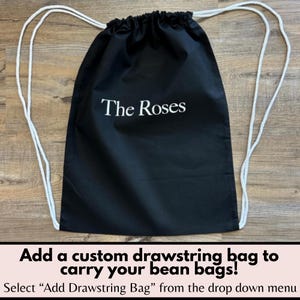 May include: Black drawstring bag with white rope straps. The text "The Roses" is printed in white on the front. The bottom of the image has text that reads "Add a custom drawstring bag to carry your bean bags!"